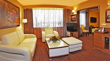 Habitación de hotel con sofá, mesa de centro con flores, televisor y escritorio con silla.