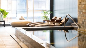 Un área de piscina interior moderna con sillones de descanso y una pared de piedra.