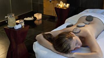 A spa setting with a massage table, a stone massage, candles, and a water pitcher.