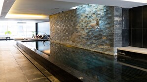 Un área de piscina interior moderna con una pared de piedra y una piscina larga y estrecha.