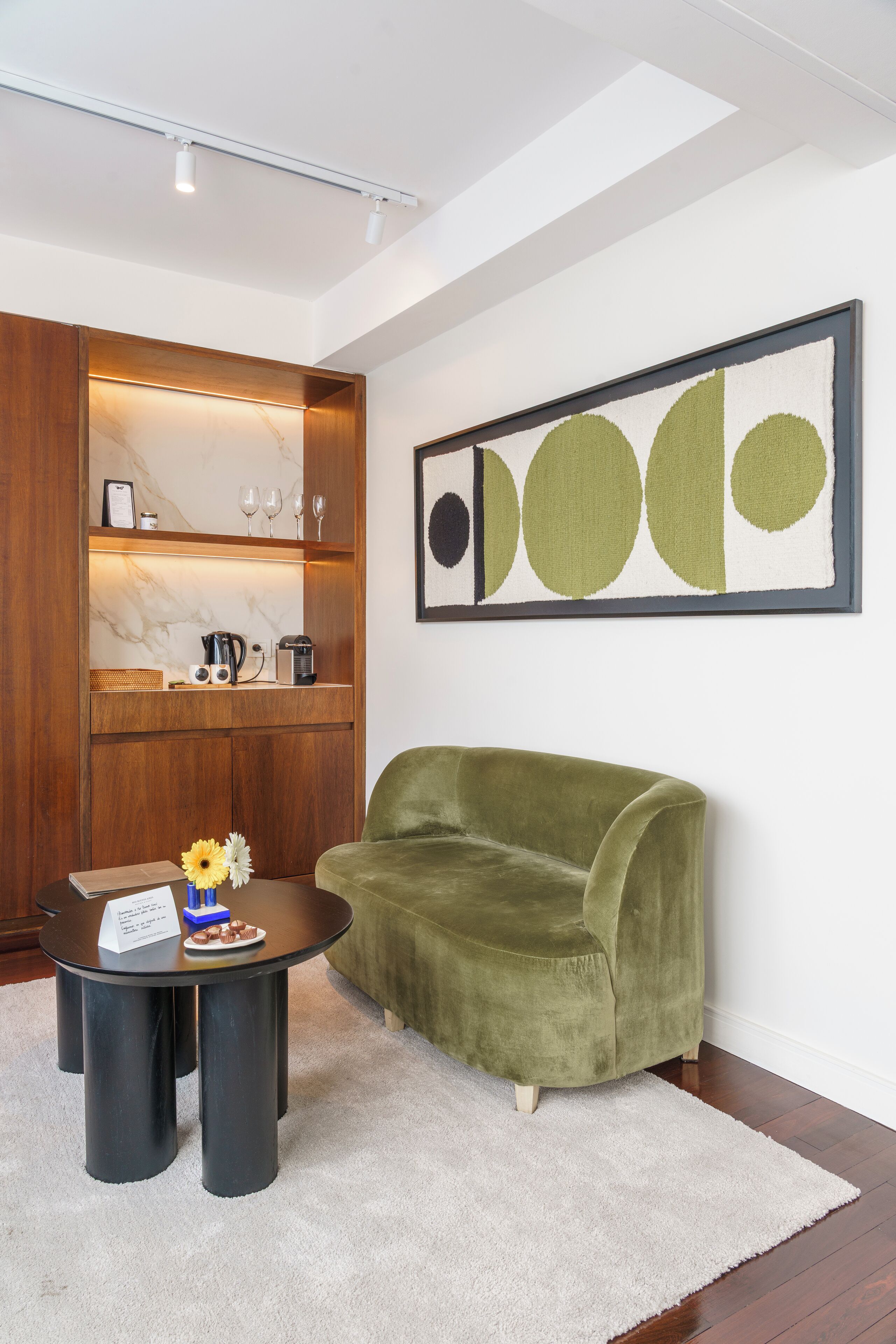A modern living room with a green sofa, a coffee table, and a sideboard with kitchen appliances.