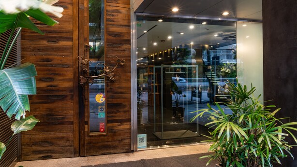 Una entrada de hotel moderna con puerta de madera, vidrio y plantas de interior.