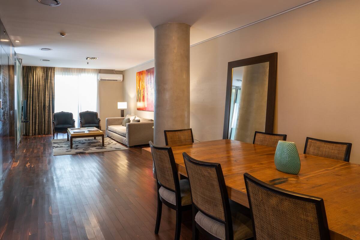 A spacious living room with a wooden dining table, comfortable seating, and a large mirror.