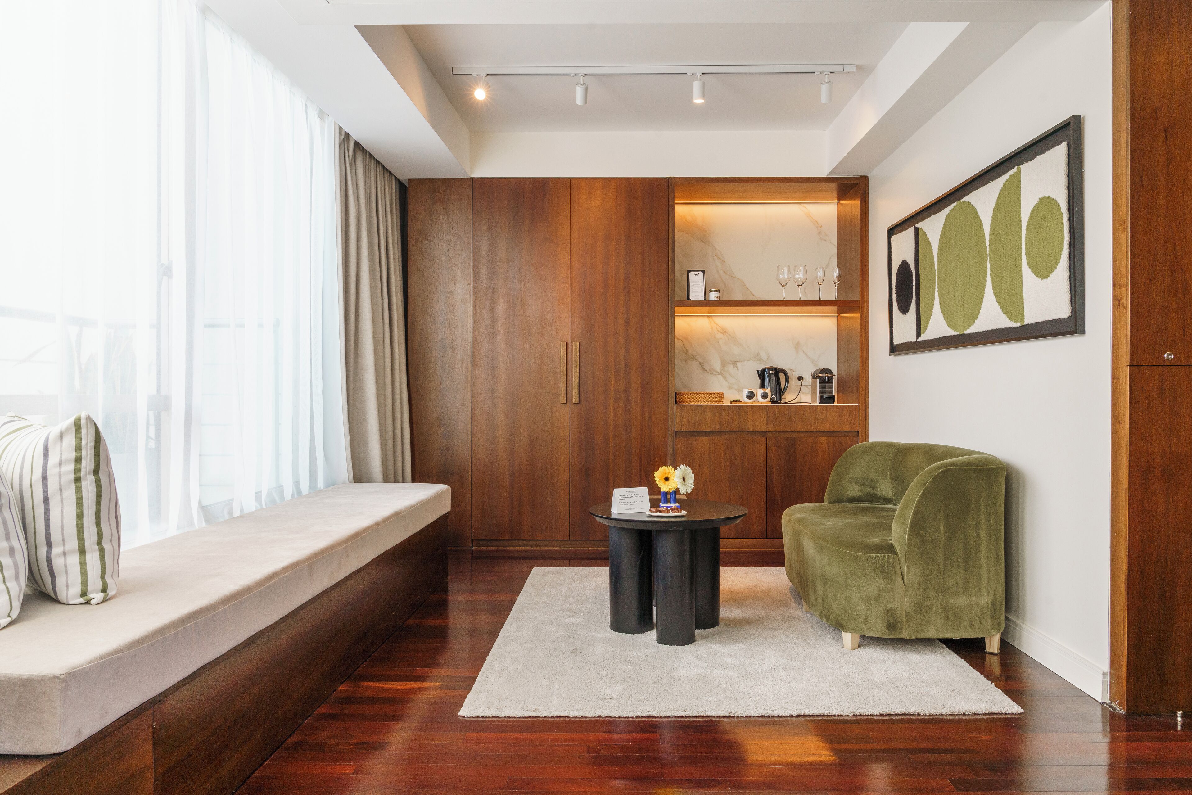 A modern living room with a wooden bench, a green armchair, a small round table with a vase, and a marble backsplash in the background.