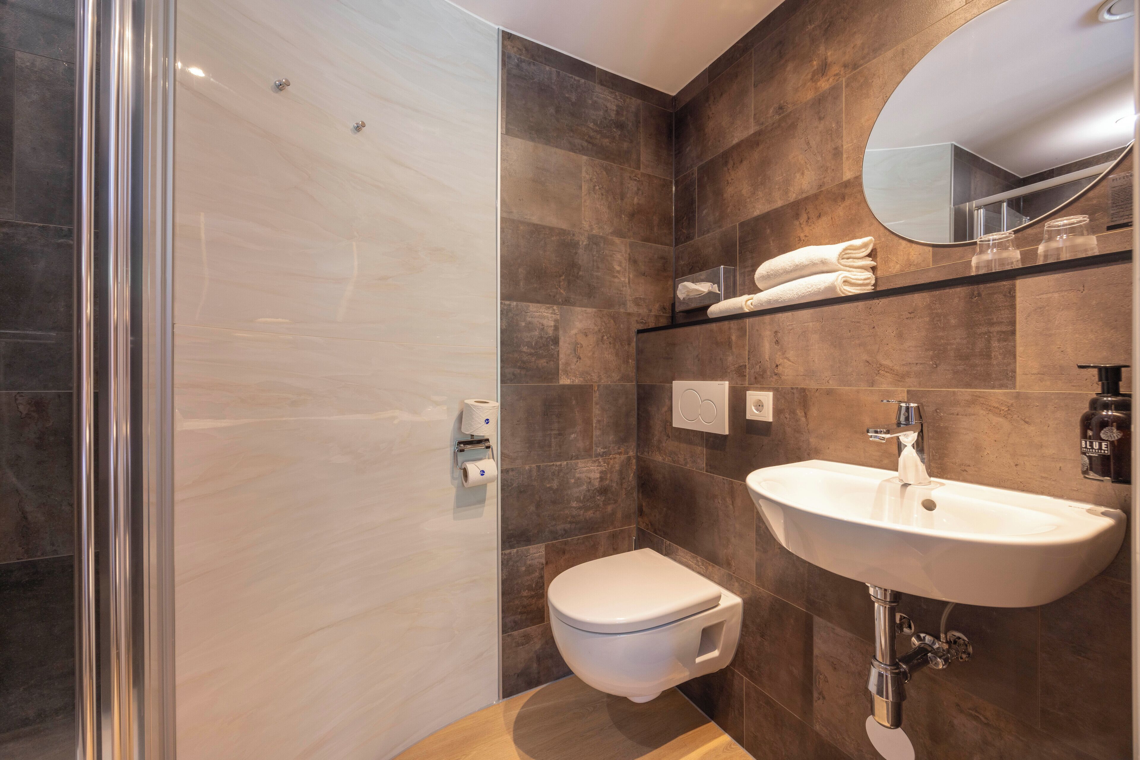 A modern bathroom with a glass shower enclosure, a white toilet, and a sink with a mirror above it.