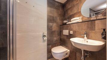 A modern bathroom with a glass shower enclosure, a white toilet, and a sink with a mirror above it.