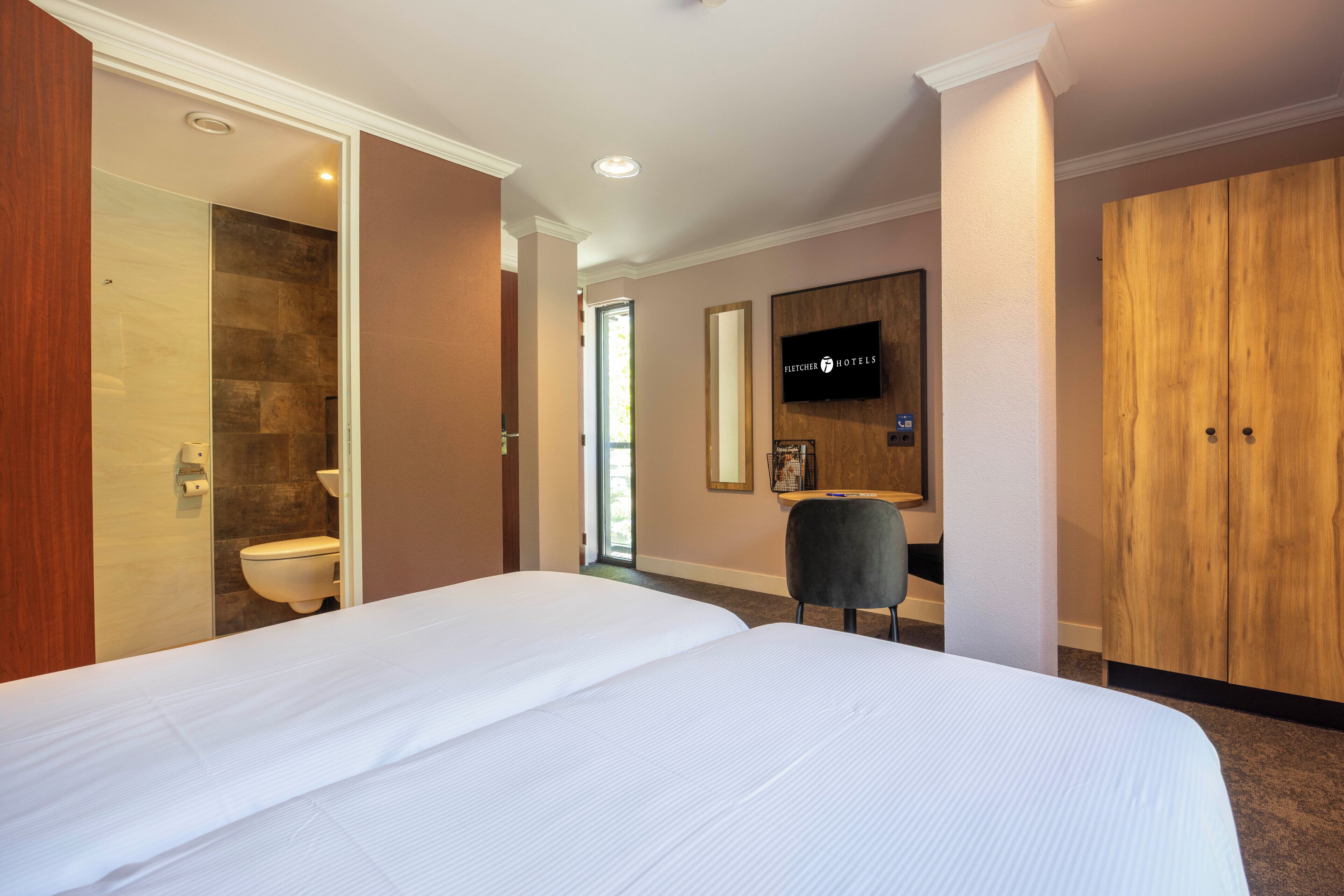 Habitación de hotel con una cama grande, un armario de madera, un televisor y un baño con pared de piedra y un inodoro.