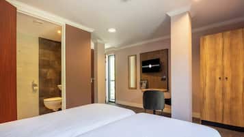 Habitación de hotel con una cama grande, un armario de madera, un televisor y un baño con pared de piedra y un inodoro.