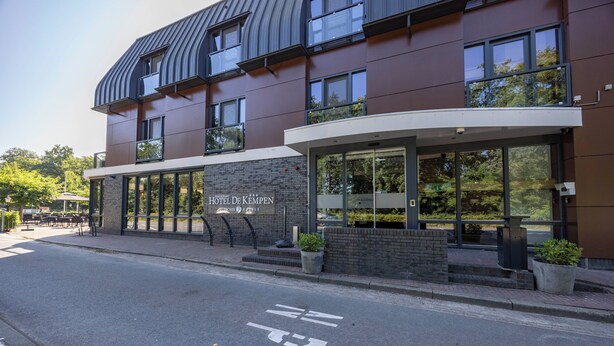 A modern hotel with a curved roof, large windows, and a sign reading "Hotel De Kempen."