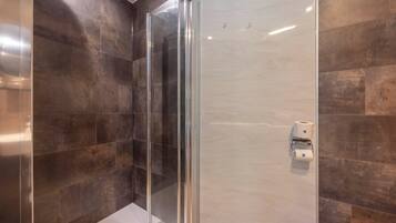 A modern bathroom with a glass-enclosed shower, dark tiled walls, and a toilet paper dispenser.
