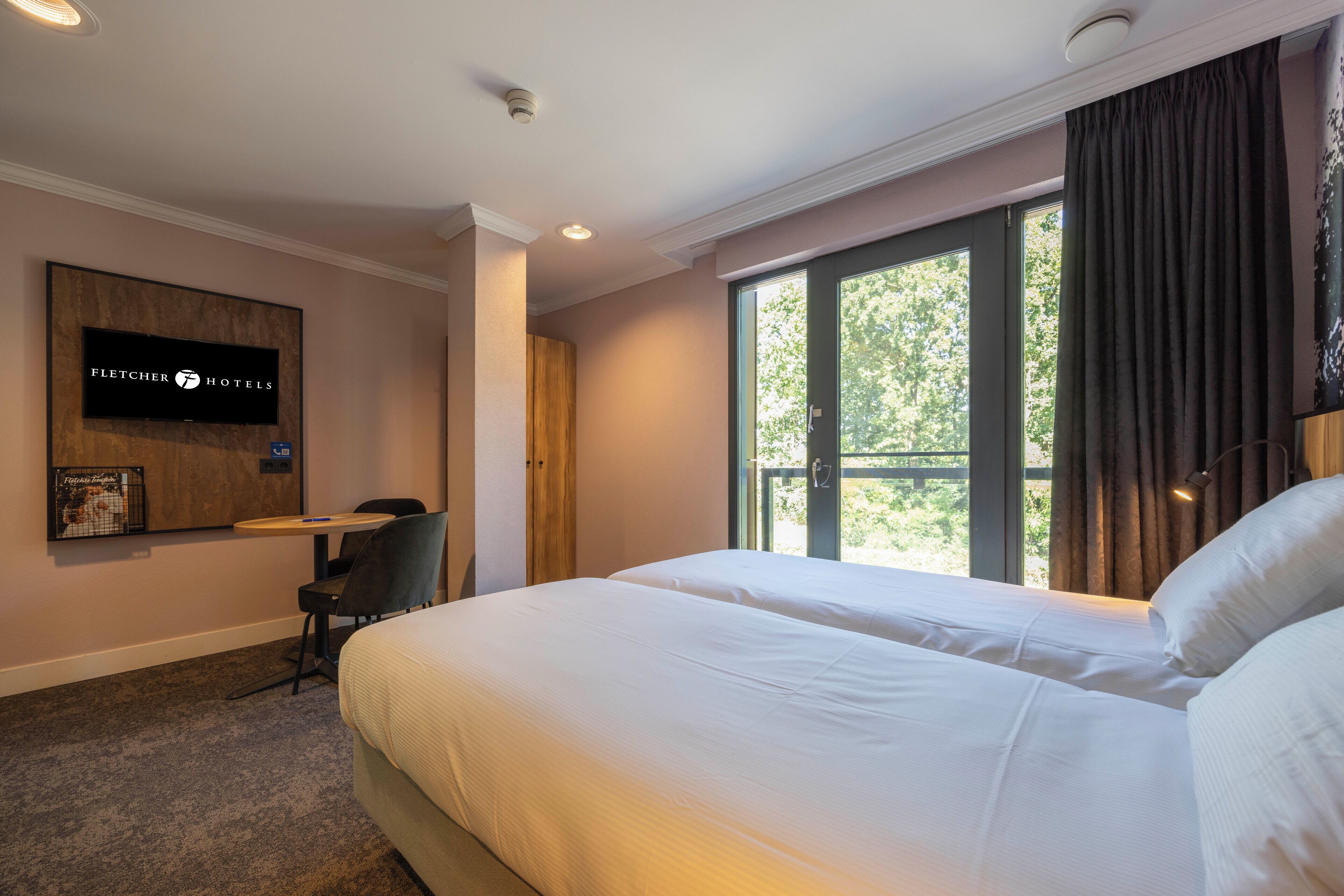 Une chambre d’hôtel équipée d’un lit, d’un bureau, d’une chaise, d’une télévision et d’une fenêtre avec des rideaux.