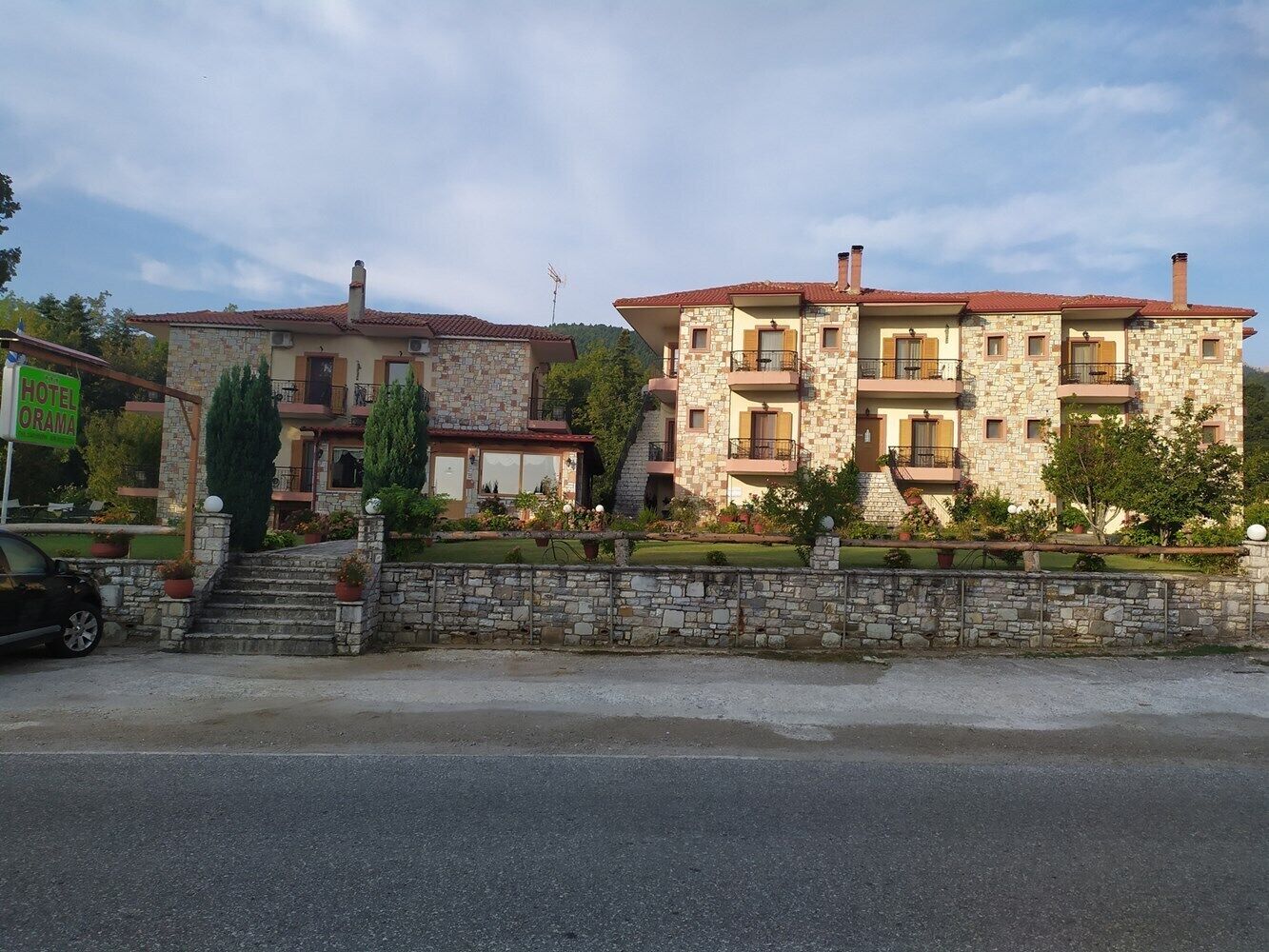 Un edificio de dos plantas de piedra con techo de tejas rojas, una escalera de piedra que lleva a la entrada y un cartel que indica que es un hotel.