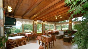 Een restaurant met houten tafels en stoelen, een televisie aan de muur en uitzicht op het omliggende landschap.