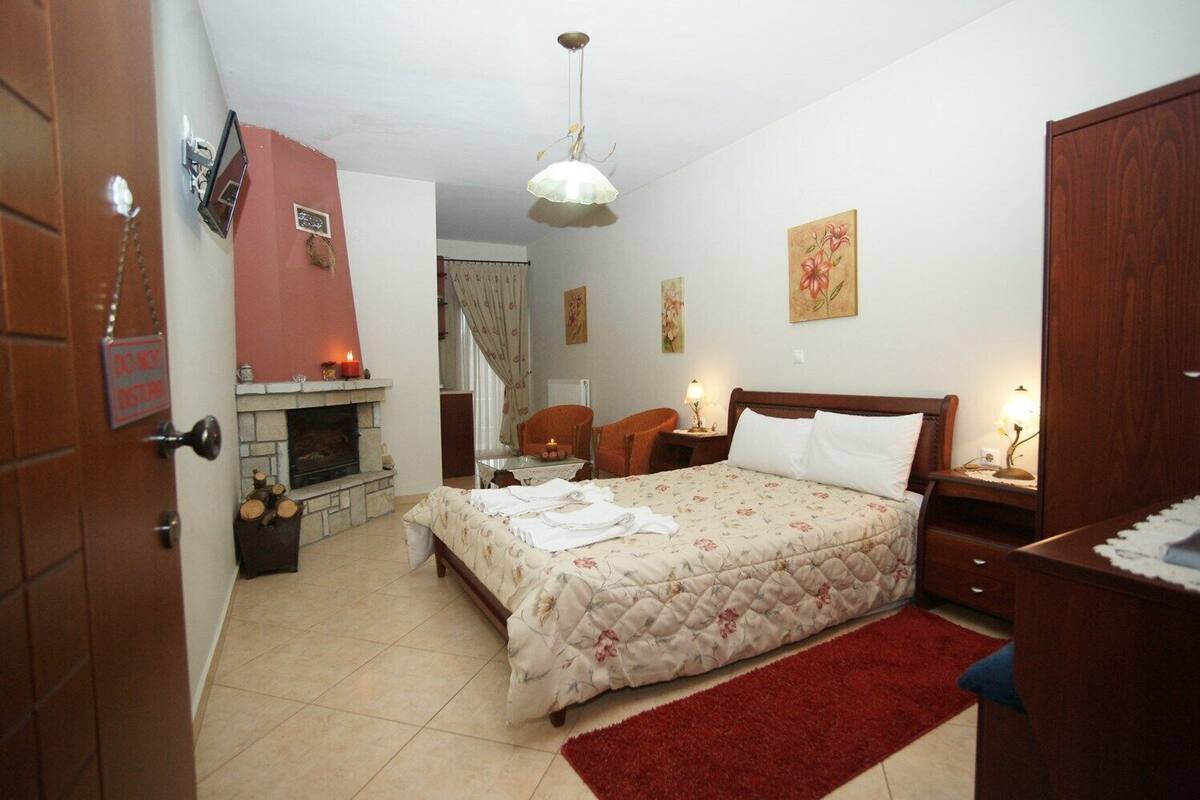 Quarto com cama, mesa de cabeceira, cadeira, lareira e porta.
