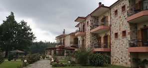 A multi-story building with stone facade and balconies, surrounded by a garden with various plants and a gazebo.