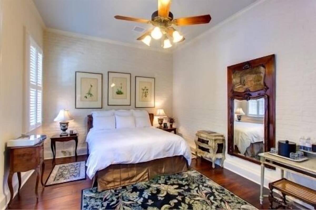 A bedroom with a bed, bedside tables, a mirror, and framed artwork on the wall.