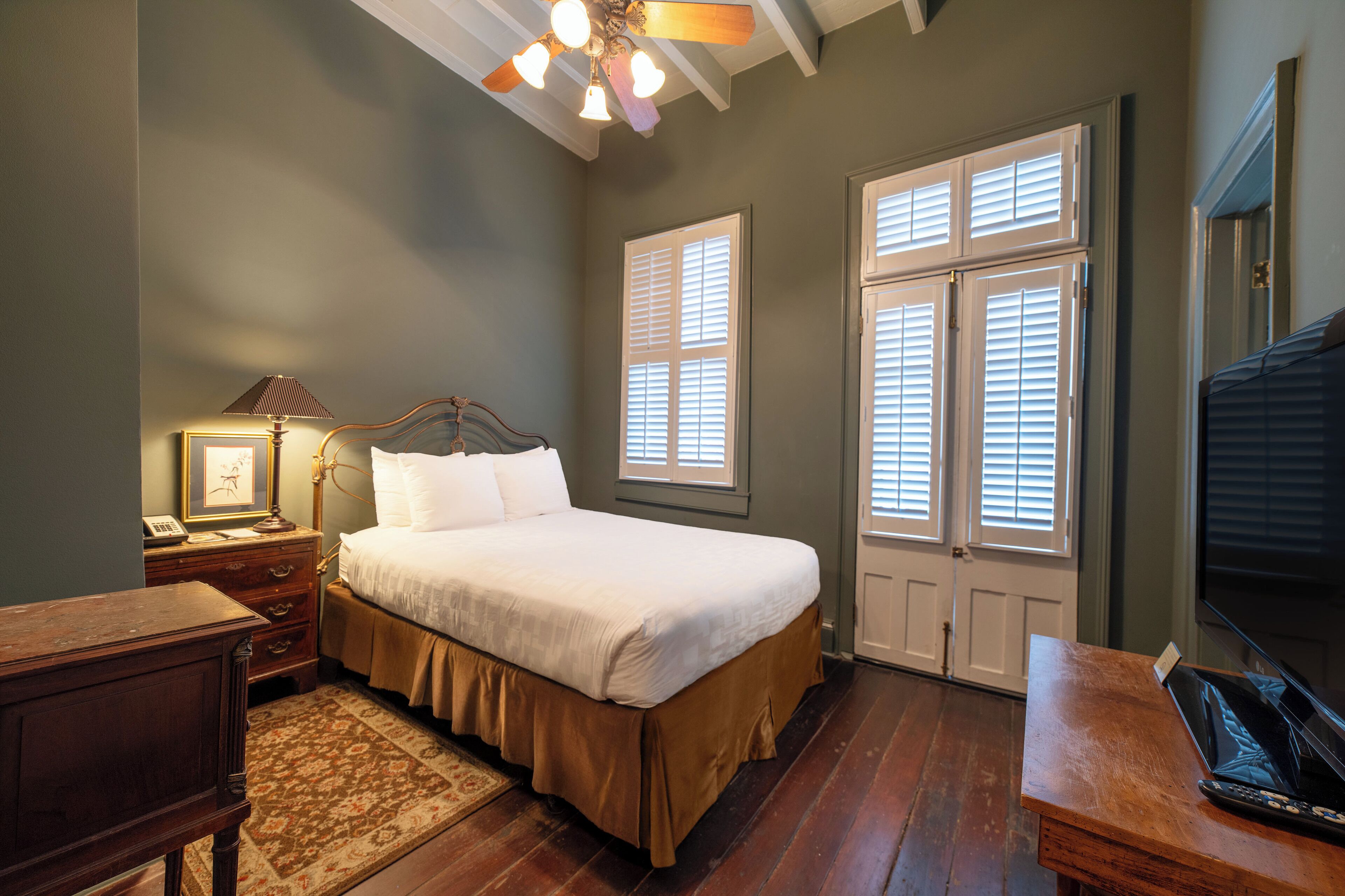 A bedroom with a bed, wooden nightstand, lamp, and a desk with a computer.