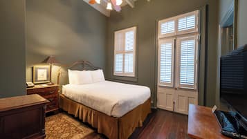 A bedroom with a bed, wooden nightstand, lamp, and a desk with a computer.