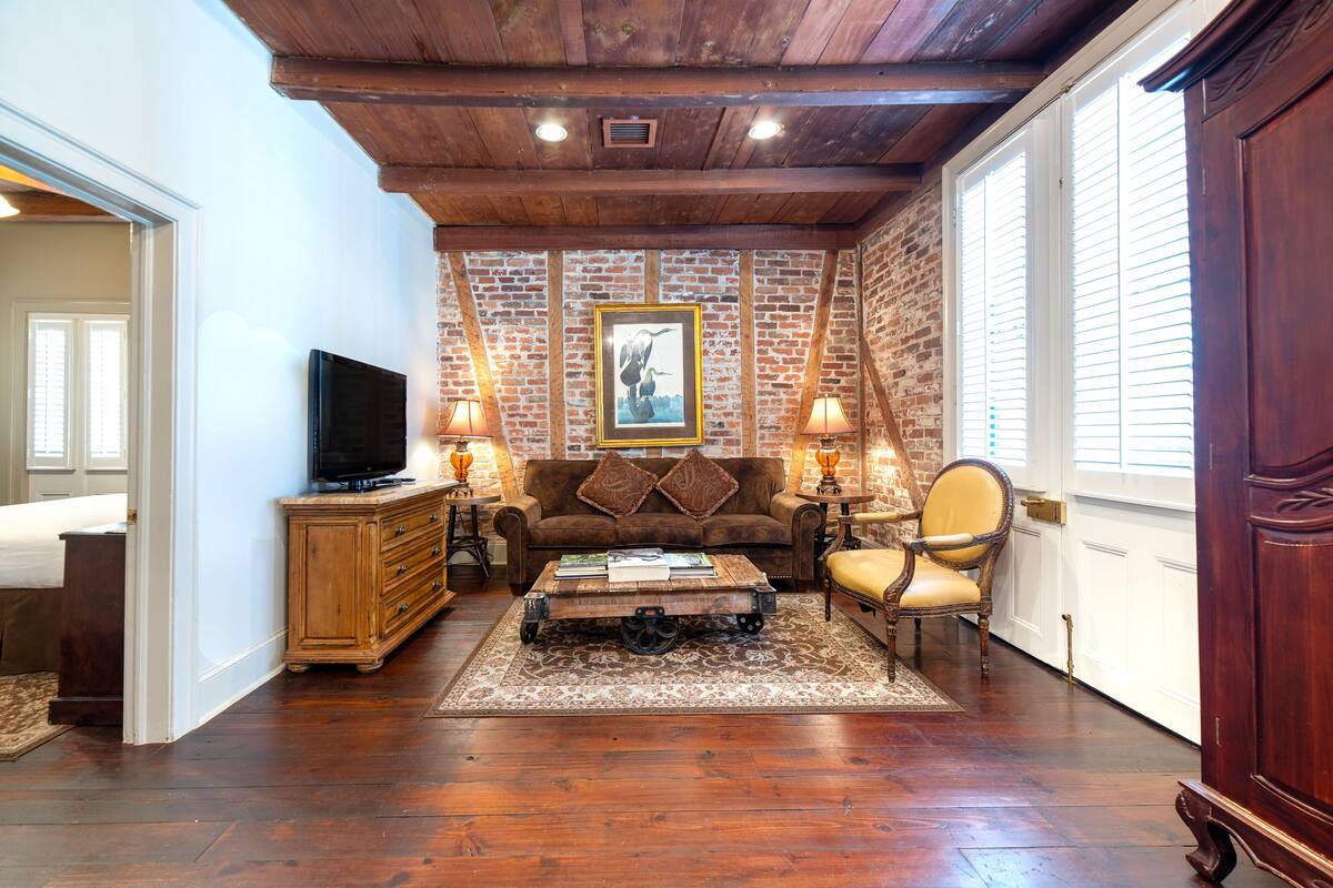 A living room with a brick wall, wooden ceiling, a sofa, a coffee table, a TV, and two lamps.