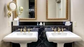 Een badkamer met twee witte wastafels op voet, zwarte marmeren tegels, gouden details en wandlampen.
