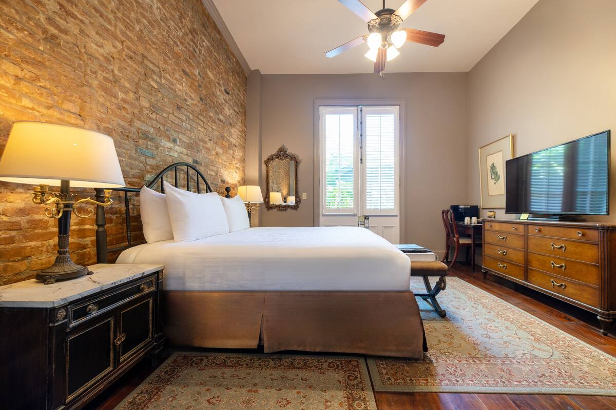A bedroom with a large bed, a dresser, a television, and a brick wall.