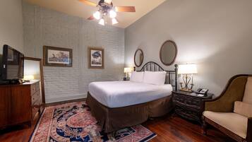 A bedroom with a bed, a wooden dresser, a chair, a nightstand with a lamp, and a ceiling fan.