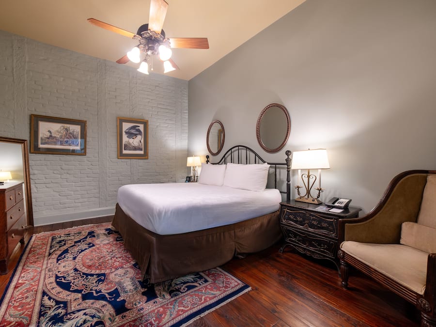 A bedroom with a bed, a wooden dresser, a chair, a nightstand with a lamp, and a ceiling fan.