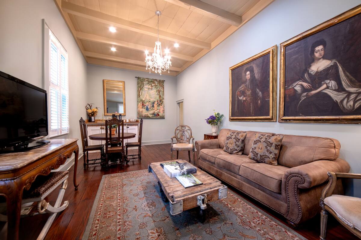 A living room with a television, a wooden coffee table, a sofa, a chandelier, and two paintings on the wall.