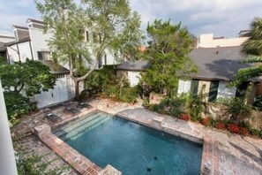 A swimming pool surrounded by a stone deck, with trees and a white building in the background.
