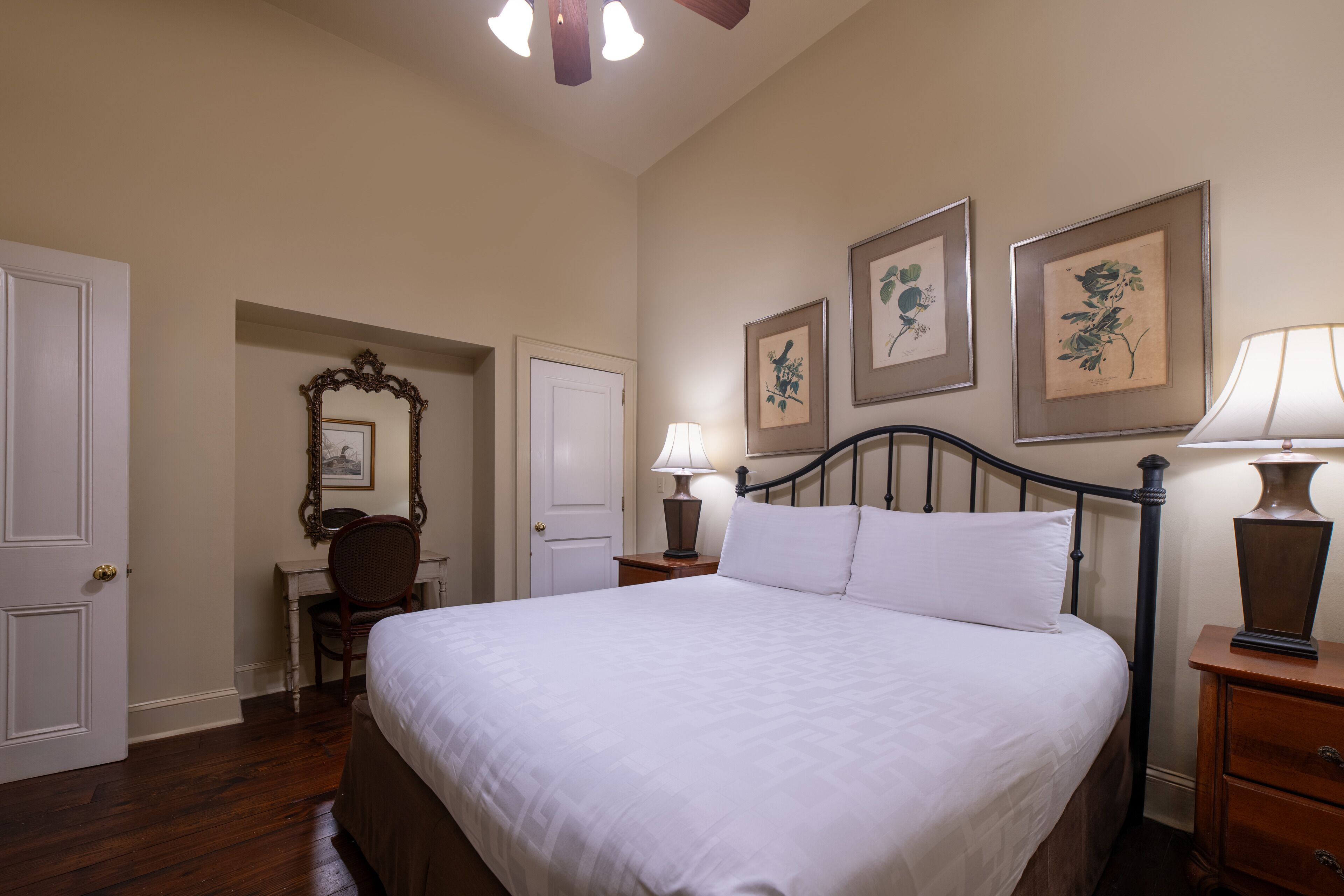 A bedroom with a large bed, a desk with a chair, a dresser, and framed floral artwork on the walls.