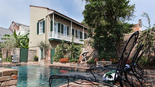 A pool area with a lounge chair and a small fountain, surrounded by a brick wall and greenery. - Audubon Cottages (New Orleans)