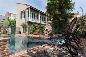A pool area with a lounge chair and a small fountain, surrounded by a brick wall and greenery. - Audubon Cottages (New Orleans)