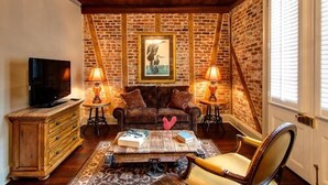 A cozy living room with a brick wall, a television, two lamps, a sofa, a coffee table, and a chair. - Audubon Cottages (New Orleans)