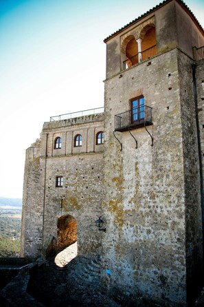 Un bâtiment historique en pierre, doté de fenêtres en arc de cercle, d’un balcon et d’une petite porte.