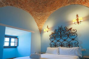 Une chambre à coucher avec un plafond incurvé, un lit recouvert de draps blancs et des lampes fixées au mur.