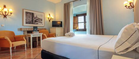 A hotel room with a bed, a desk, a chair, a television, and a framed picture on the wall.