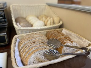 Une miche de pain tranché dans un panier en osier, accompagnée d’un couteau à pain et de pinces.