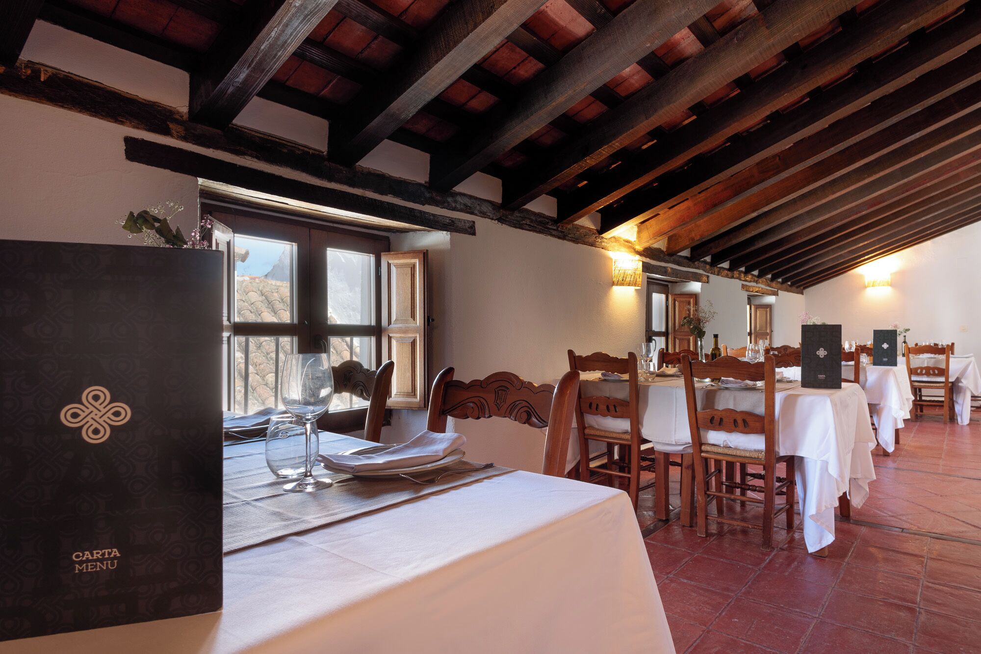 A restaurant with wooden beams, white tablecloths, and a menu stand.