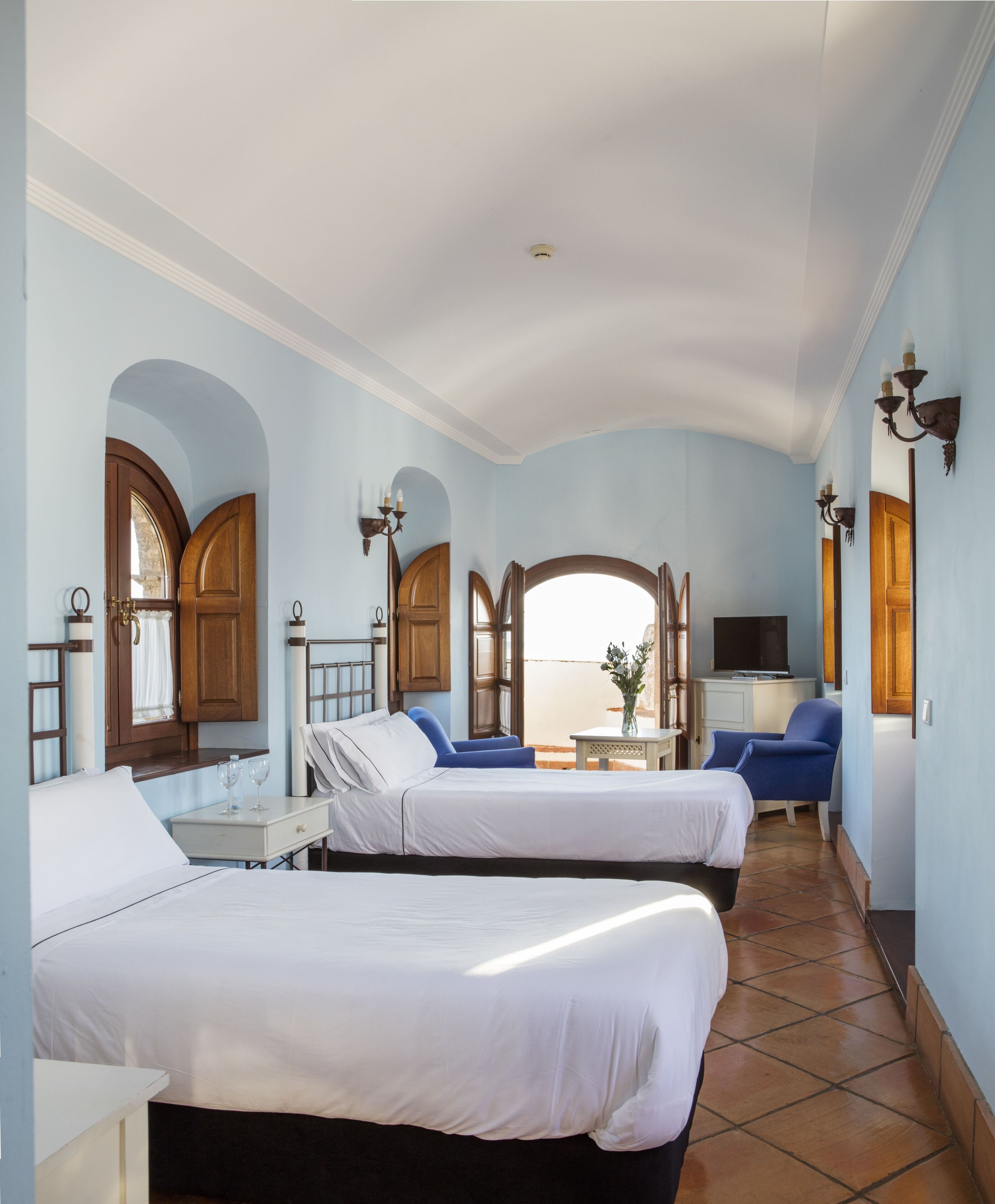 A hotel room with two beds, a TV, a small table, and a view of the sea.