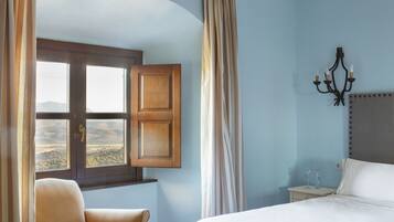 Un dormitorio con una cama grande, una silla, una mesita de noche, una ventana con cortinas y vistas al exterior.