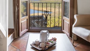 A room with a balcony, a table with a tray of items, and a view of a landscape with hills and a body of water. - TUGASA Castillo de Castellar (Castellar de la Frontera)