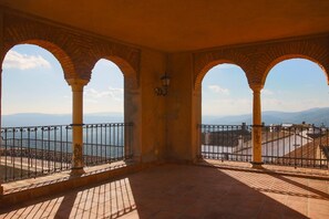 Une terrasse couverte, dotée de colonnes en briques en forme d’arc, d’une rambarde en métal et offrant une vue sur des montagnes lointaines et une étendue d’eau.