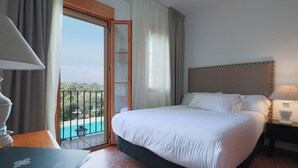 A hotel room with a bed, a desk, a lamp, and a view of a pool and greenery. - TUGASA El Almendral (Setenil de las Bodegas)