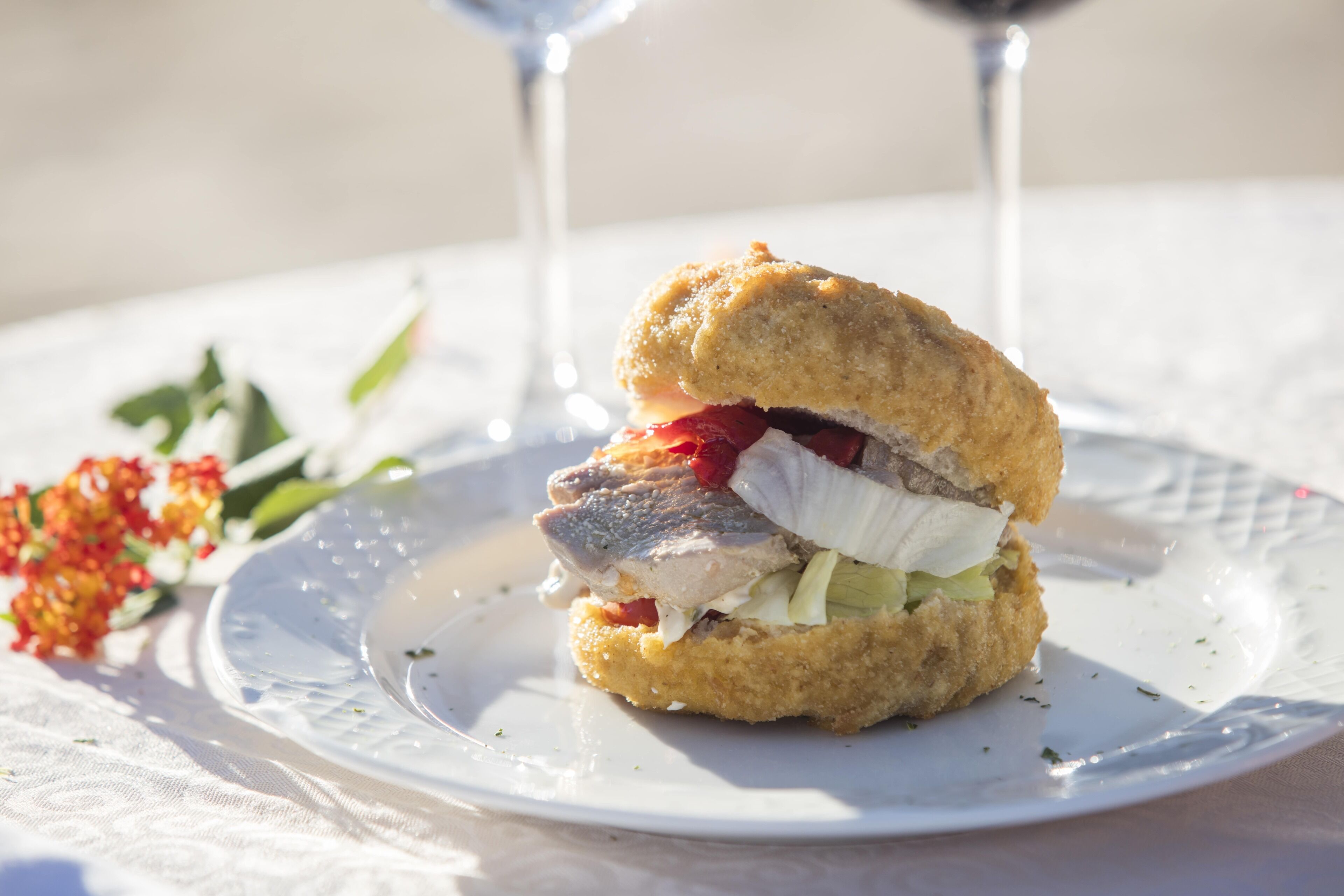 A sandwich on a white plate with a glass of red wine in the background.