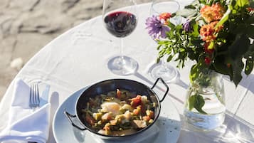 Una mesa servida con comida, copas de vino y un florero con flores.