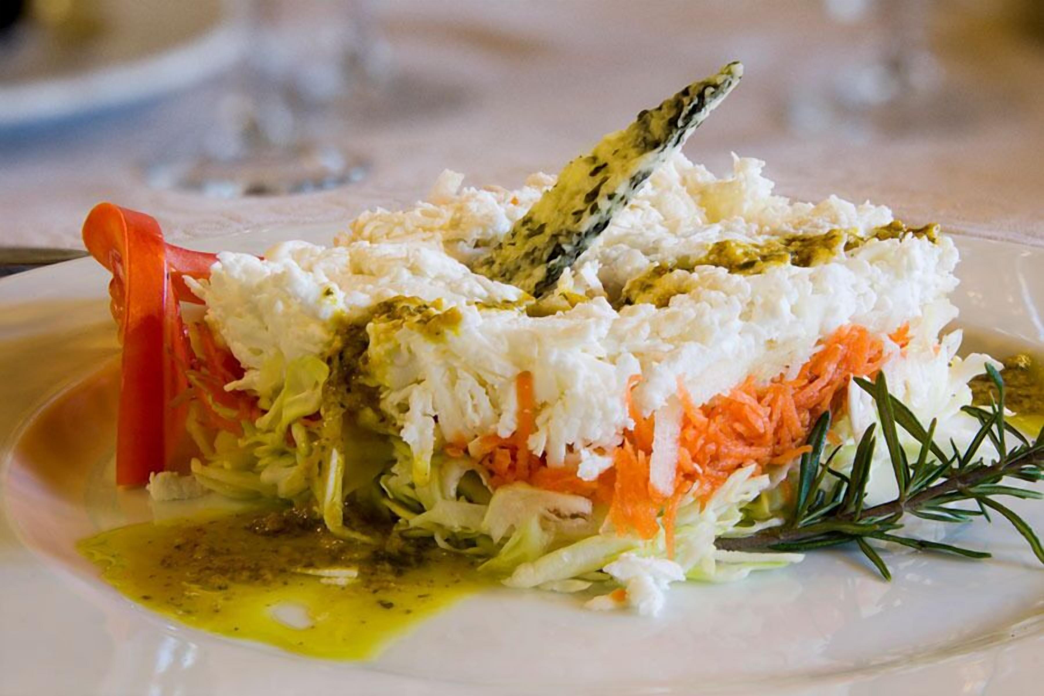 A dish with shredded vegetables, possibly carrots and cabbage, topped with a creamy substance and garnished with a sprig of rosemary.