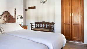 A bedroom with a bed, a wooden bench, a wardrobe, and a wall-mounted air conditioner. - TUGASA Hotel La Posada (Villaluenga del Rosario)