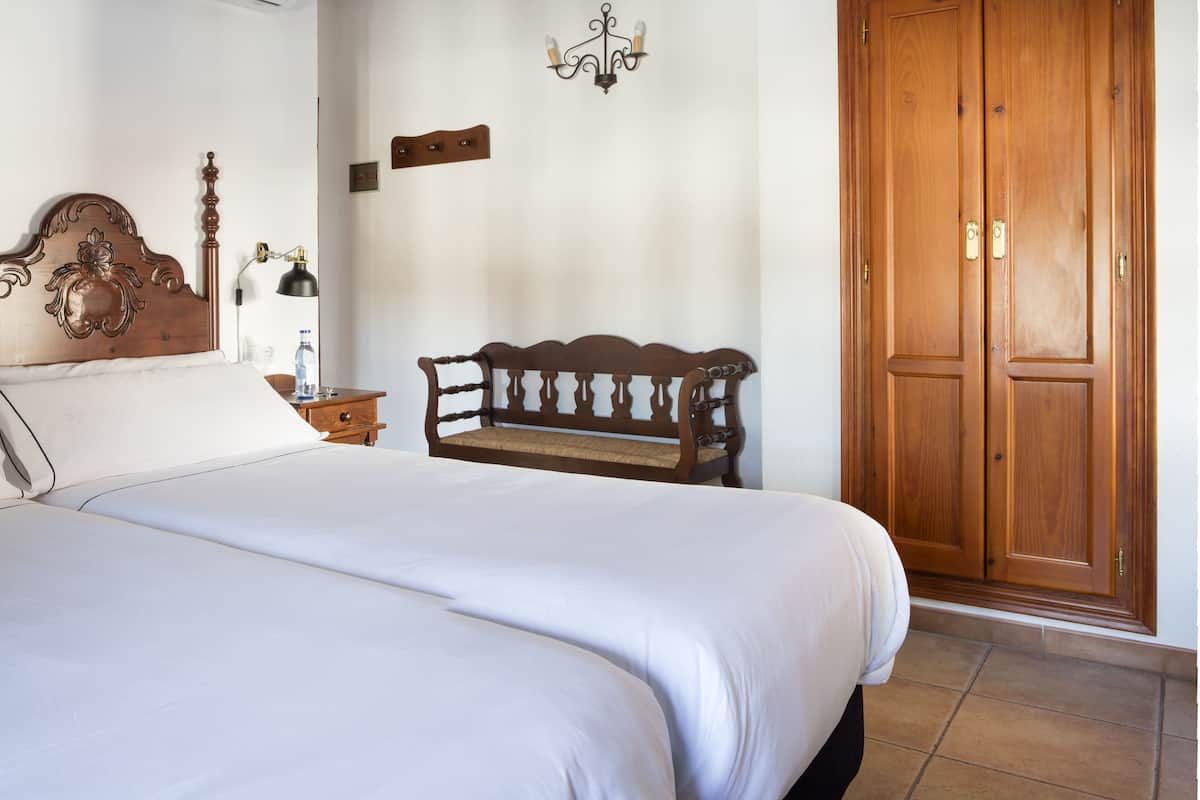 A bedroom with a bed, a wooden bench, a wardrobe, and a wall-mounted air conditioner.