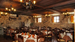 A restaurant with stone walls, wooden tables, and multiple chandeliers. - TUGASA Hotel La Posada (Villaluenga del Rosario)