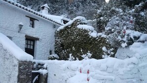 A snow-covered building with a stone wall and a wooden door. - TUGASA Hotel La Posada (Villaluenga del Rosario)